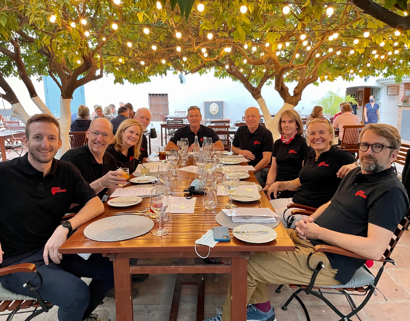 Moto Adventura tour group dinner under string lights on outdoor terrace, Spain